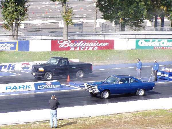 Blue classic car and black pickup truck at drag strip