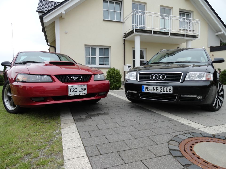 Red 2003 Ford Mustang GT parked next to a black Audi A6 in front of a house