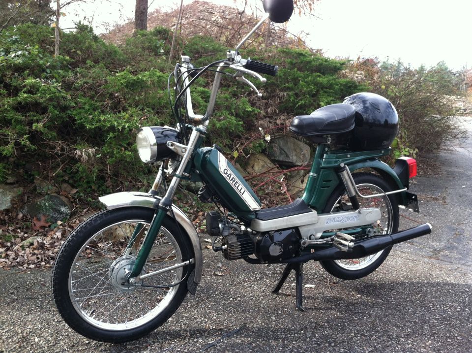 Green Garelli moped with chrome fenders and handlebars, black seat, and a black helmet on the rear rack