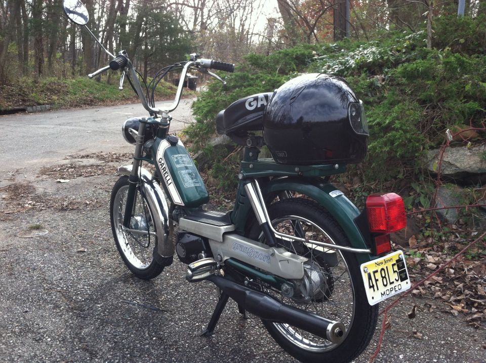 Green moped with a black helmet on the seat and a New Jersey license plate
