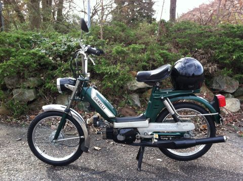 1981 Garelli Rally Sport - A green Garelli moped with a black helmet is parked on a gravel surface with a wooded background.