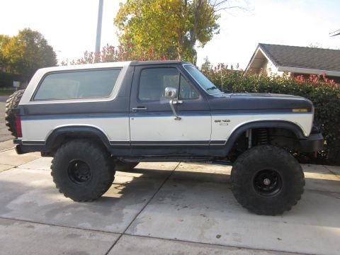 1985 Ford Bronco - This lifted Ford Bronco has a two-tone paint scheme and is parked on a paved surface.