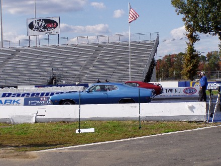 1999 Ford Crown Victoria - Two cars line up at the start of a drag race, with spectators in the stands.