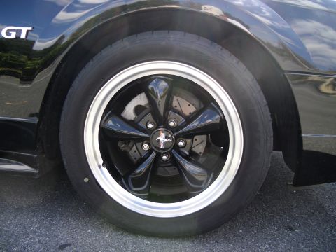 1978 Ford Bronco - Close-up of a black five-spoke wheel with a silver trim ring on a black car. The Mustang logo is visible on the center cap.