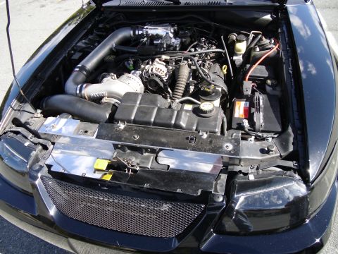 1978 Ford Bronco - The engine bay of a black car features a supercharger and custom intake system.