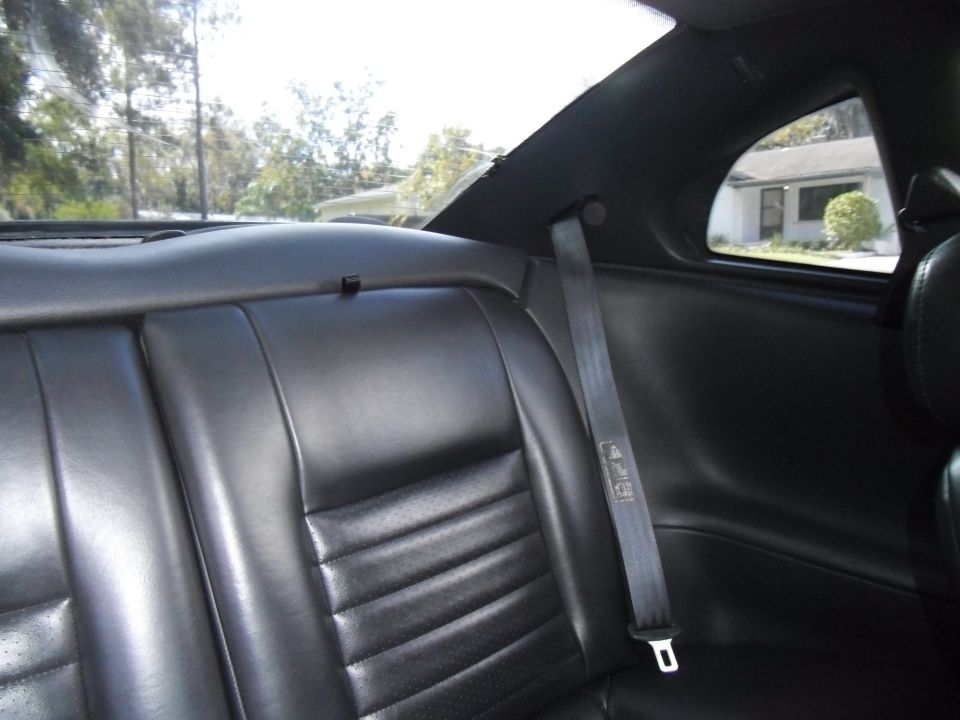 Rear leather seats and seatbelt inside a car, view through the rear window shows a house