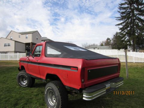 1979 Ford Bronco - Red lifted Ford Bronco with black soft top and chrome wheels parked on grass in front of houses, dated 11/13/2011.