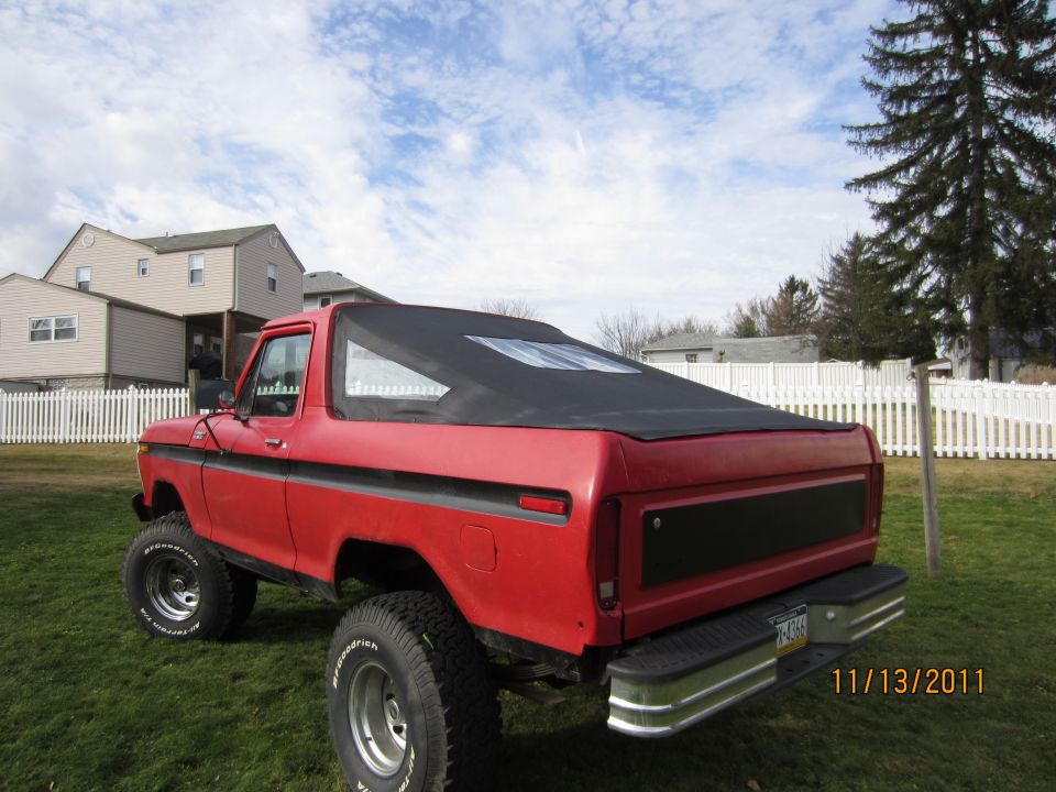 Rear quarter of red lifted 1978-79 Ford Bronco with black soft top in a yard