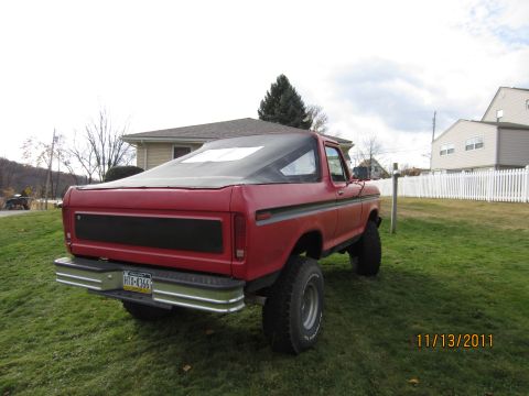 1979 Ford Bronco - This 1979 Ford Bronco features a red exterior, a soft top, and aftermarket wheels, seen from the rear.