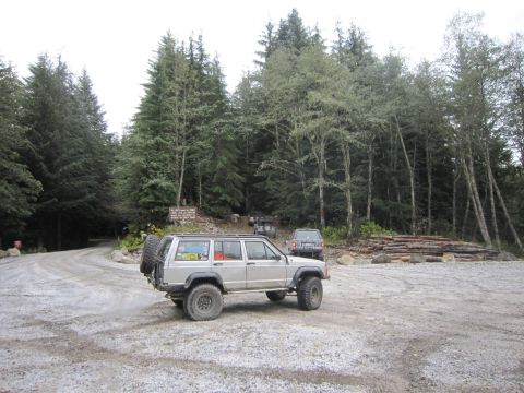 2008 Jeep Wrangler - Multiple Jeeps and an SUV are parked on a gravel road near a forest with cut logs.