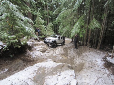 2008 Jeep Wrangler - A white 2007 Jeep Wrangler tackles a challenging, snow-dusted trail through a dense forest.