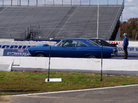 1999 Ford Crown Victoria - A blue 1966 Ford Fairlane sedan is parked on a drag strip next to another vehicle, with bleachers in the background.