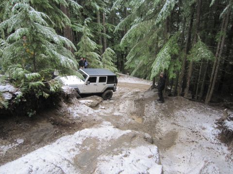 2008 Jeep Wrangler - A white Jeep Wrangler navigates a challenging off-road trail with patches of snow and mud.
