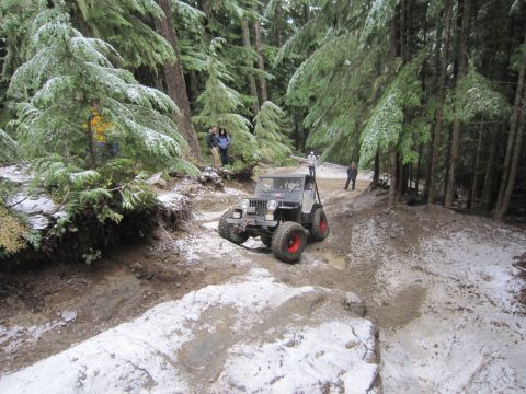 2008 Jeep Wrangler - A gray Jeep Wrangler navigates a snowy and muddy off-road trail through a dense forest.