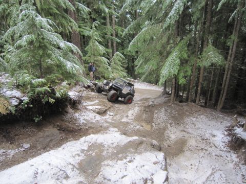 2008 Jeep Wrangler - Two off-road vehicles traverse a challenging, snow-dusted trail in a dense forest.