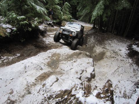 2008 Jeep Wrangler - A white off-road vehicle navigates a challenging, snowy trail through a dense forest.
