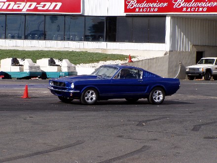 1999 Ford Crown Victoria - A blue classic Ford Mustang is on a race track with a white Jeep Cherokee parked behind it.
