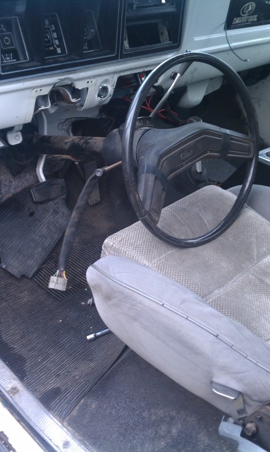 1978 Ford Bronco - The interior of a 1978 Ford Bronco shows a worn gray seat and a steering wheel with exposed wiring on the dashboard.