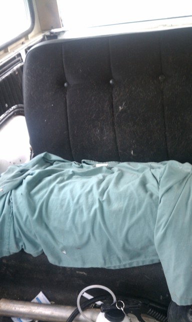 1978 Ford Bronco - The interior of a vehicle shows a tufted black seat covered by a teal shirt.