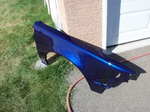 1965 Ford Fairlane - A freshly painted blue car fender is shown outdoors next to a garage.