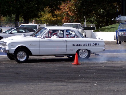 1999 Ford Crown Victoria - A white drag car performs a burnout on the track, with other vehicles visible in the background.