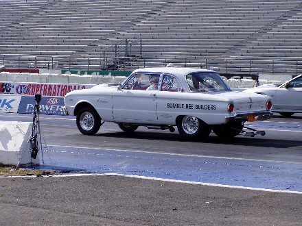 1999 Ford Crown Victoria - A white drag car is on the race track, with another vehicle partially visible to its right.