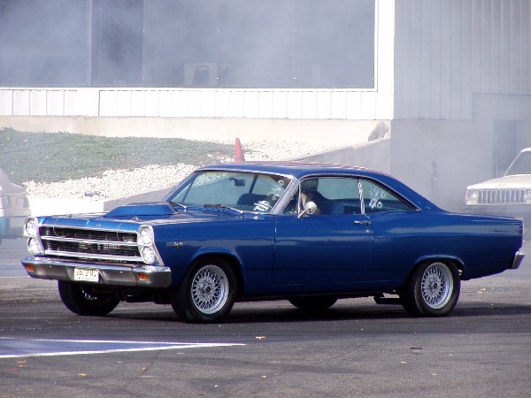 Blue 1966 Ford Fairlane coupe with a hood scoop and aftermarket wheels, seen from the front-right