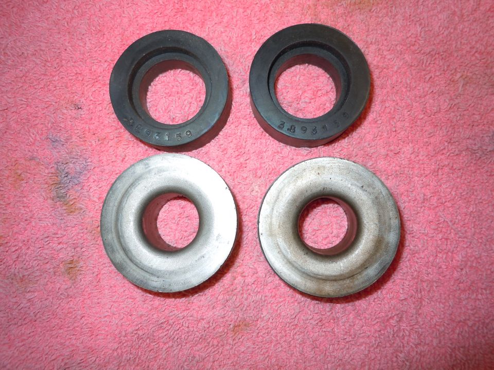 Four automotive rings, two black rubber and two silver metal, arranged in a two-by-two grid on a pink cloth
