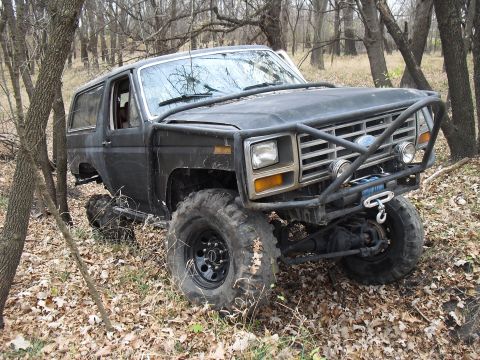 1986 Ford Bronco - This heavily modified Ford Bronco, likely from the early 1980s, navigates a wooded trail.