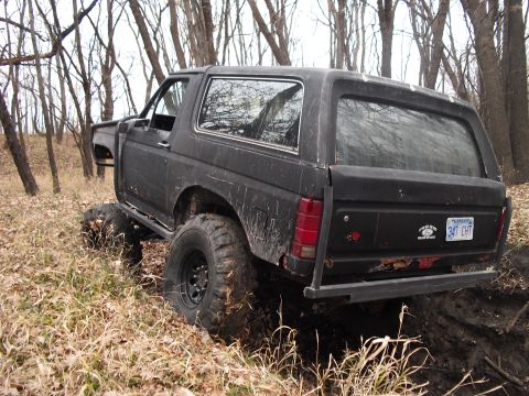 1986 Ford Bronco - This modified Ford Bronco is navigating a muddy trail through a wooded area.
