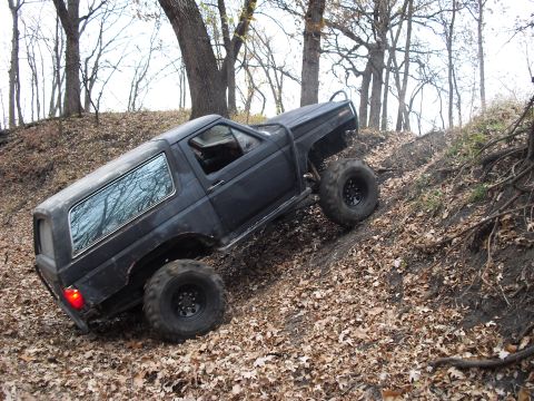 1986 Ford Bronco - A black SUV navigates a steep, muddy incline covered in fallen leaves.