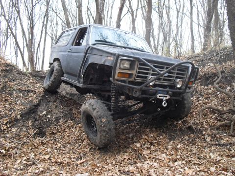 1986 Ford Bronco - This heavily modified Ford Bronco is shown off-roading on a steep, wooded incline.