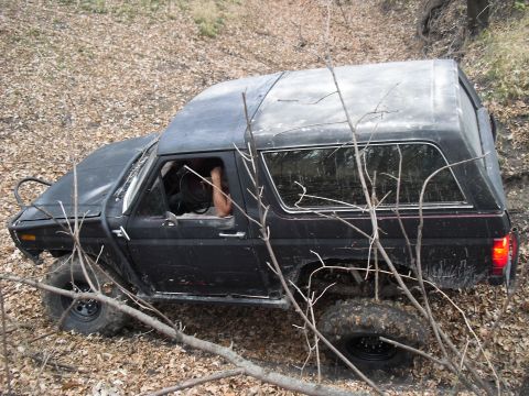 1986 Ford Bronco - This black Ford Bronco is navigating a wooded area with rough terrain.
