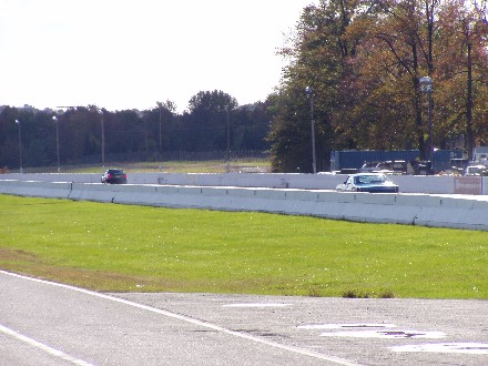 1999 Ford Crown Victoria - Two cars race on a track with a concrete barrier and grassy infield.
