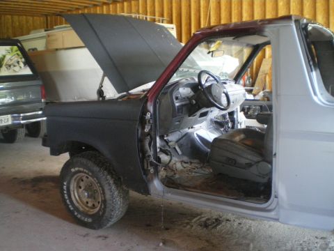 1988 Ford Bronco - A disassembled 1988 Ford Bronco sits in a garage with its hood and door open, revealing the interior.