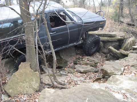 1986 Ford Bronco - Modified 1980s Ford Bronco navigating a rocky trail in a wooded area.