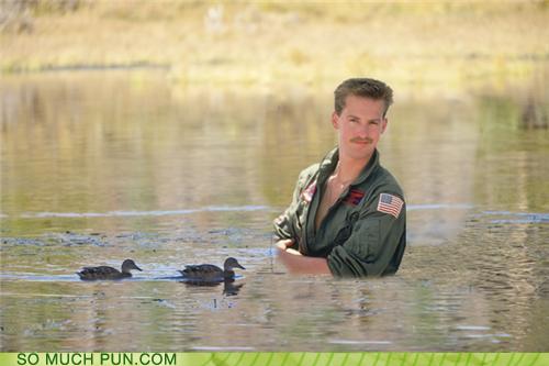 Man in a green flight suit with an American flag patch stands in water with two ducks swimming nearby. "SO MUCH PUN.COM" and "SUPERMOTORS.NET" logos are visible