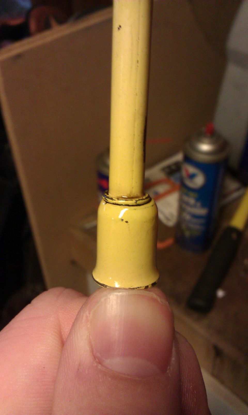 Close-up of a yellow electrical part held by a thumb, with a spray can in the background