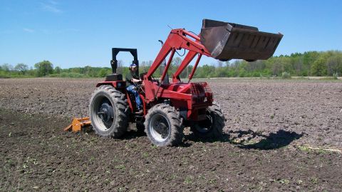 2000 Chevrolet Tahoe - A red tractor with a front loader is actively tilling a large, plowed field under a clear blue sky.