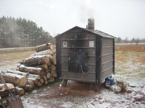 1963 Hummer H3 - A wood boiler operates in snowy conditions, with a stack of firewood nearby.