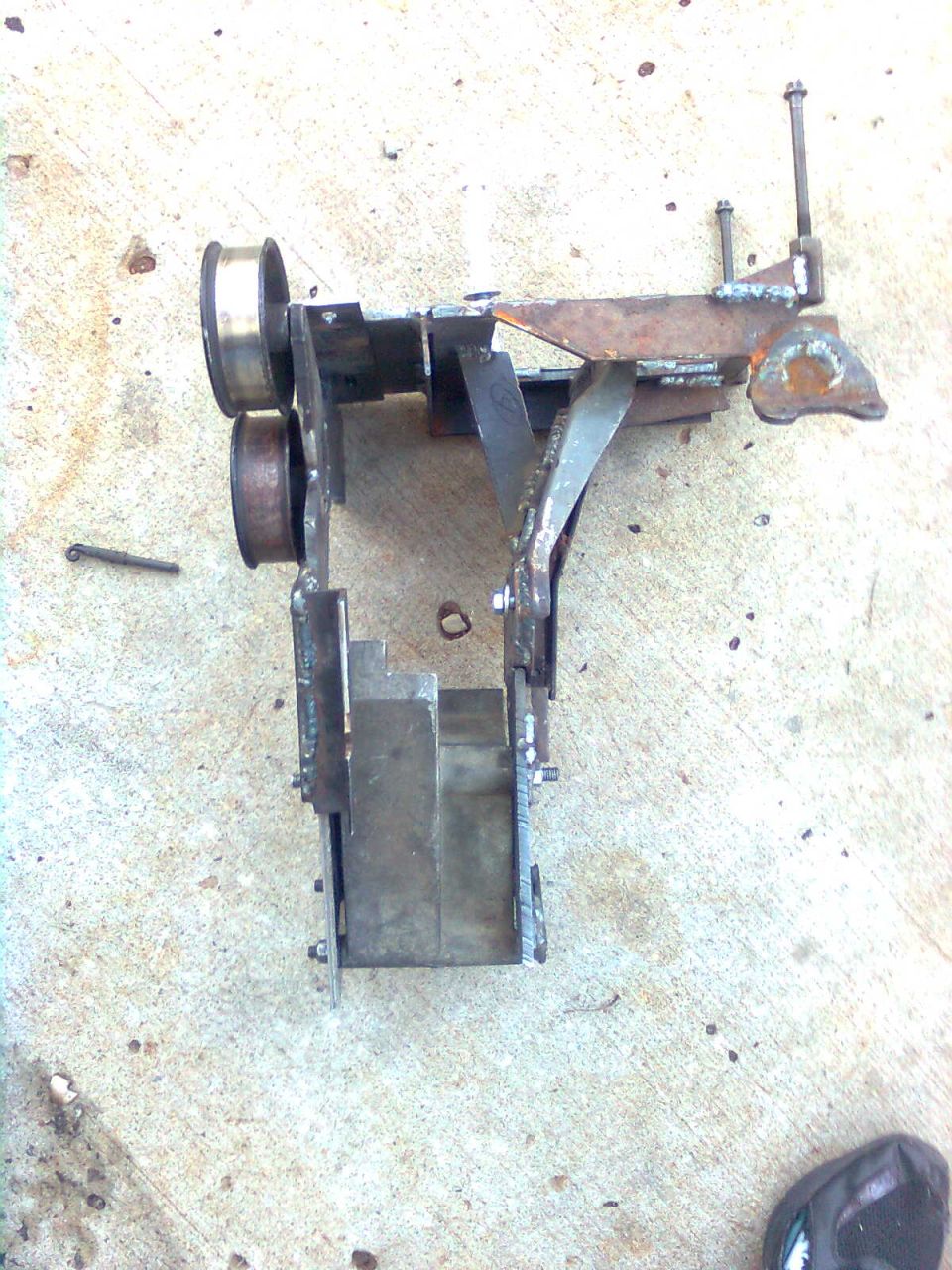 custom metal bracket with two pulleys and welded components, resting on a concrete surface