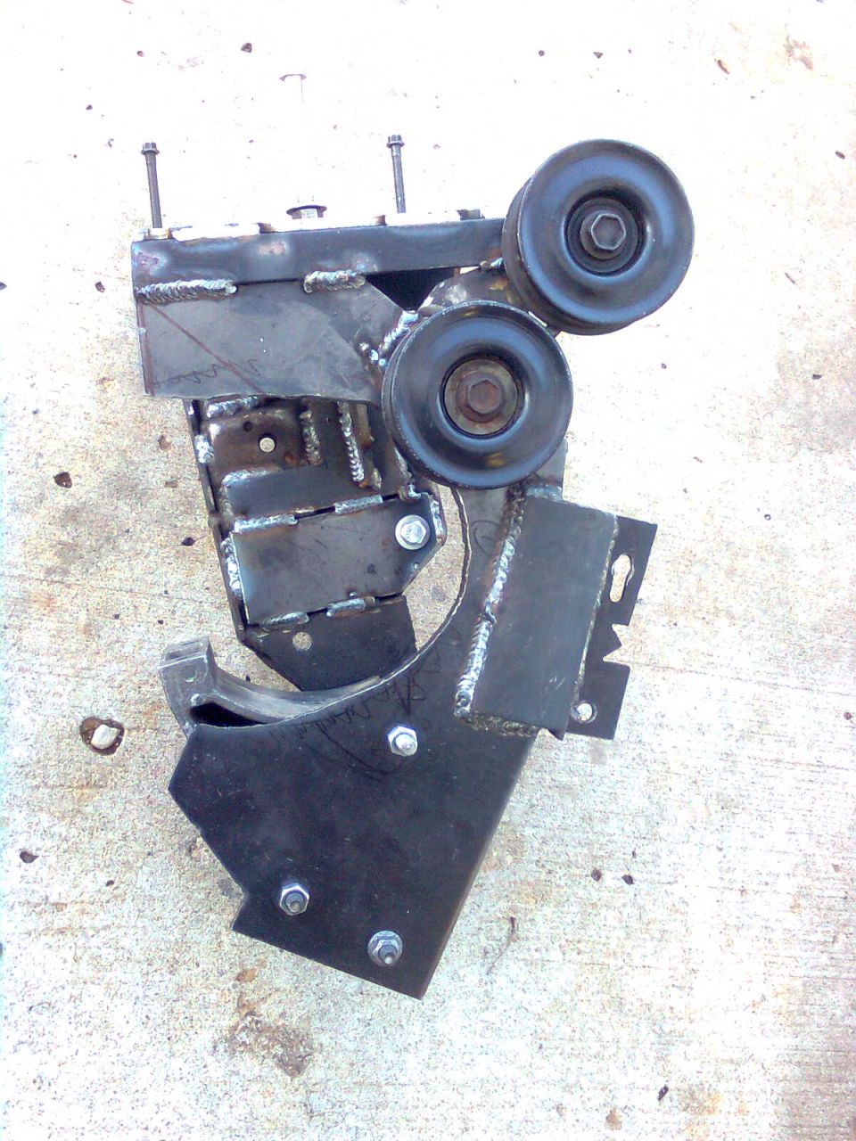 Custom metal bracket with two pulleys, bolted together with visible welds and grind marks
