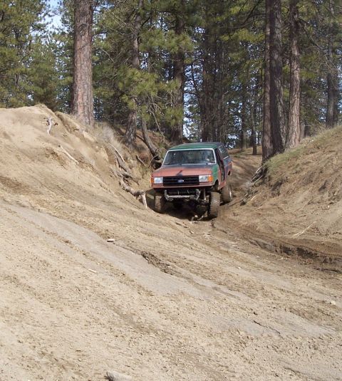 1988 Ford Bronco - This modified Ford Bronco navigates a steep, sandy trail surrounded by pine trees.