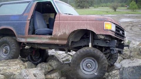 1988 Ford Bronco - This heavily modified Ford Bronco is shown off-roading over large rocks, with its doors removed.