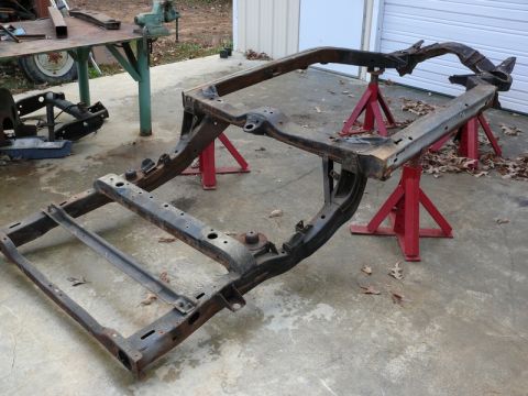 1976 Chevrolet Corvette - A rusty car frame is supported by red jack stands on a concrete surface.