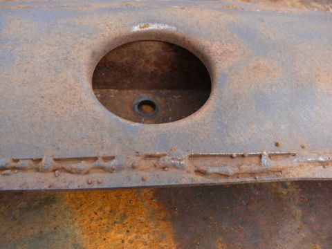1976 Chevrolet Corvette - This is a close-up view of a rusted metal component with a hole and weld seams.