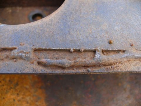 1976 Chevrolet Corvette - This image shows a close-up view of a heavily rusted metal component with distinct weld marks.