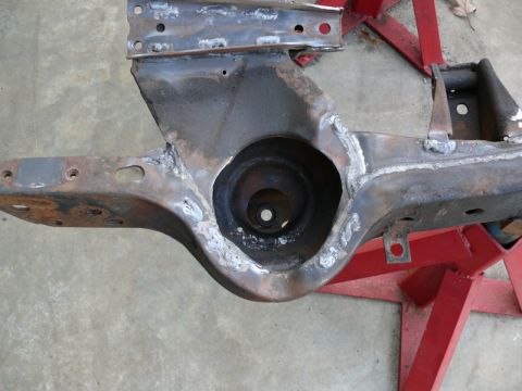 1976 Chevrolet Corvette - A section of a car's frame, showing welds and a large circular opening, is supported by red stands.