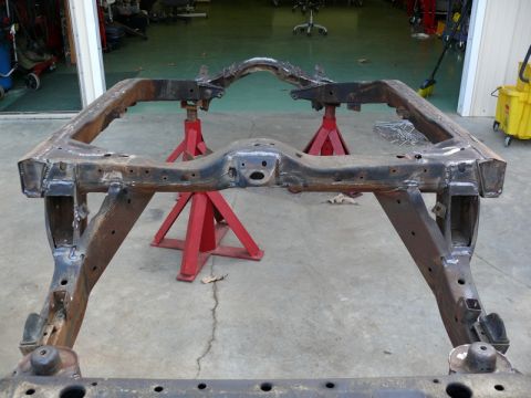 1976 Chevrolet Corvette - The bare frame of a vehicle is supported by red jack stands in a workshop setting.