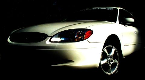 2001 Ford Taurus - A white sedan is shown from the front three-quarter view, with its headlights illuminated against a dark background.